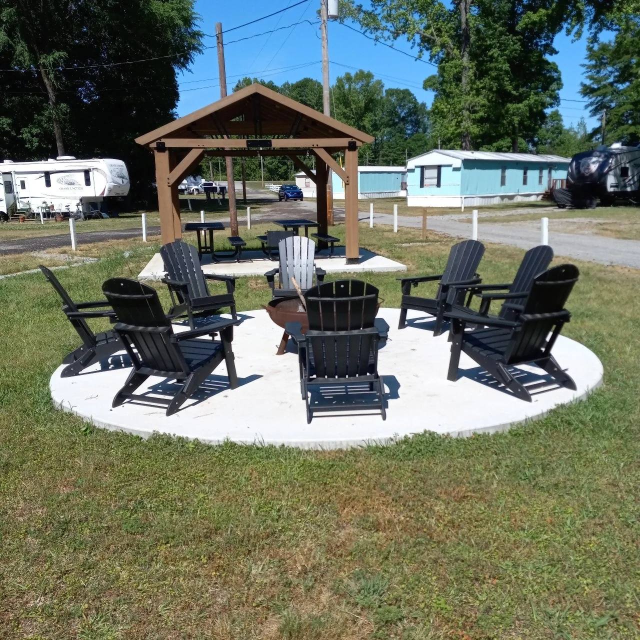 Fire pit circled by Adirondack chairs, with the pavilion behind